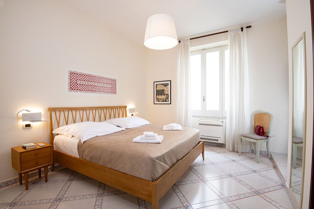 A bright, spacious bedroom with a wooden bed frame, modern amenities, and a balcony overlooking the area.