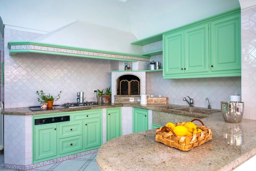 A bright turquoise kitchen with granite countertops, white diagonal tile backsplash, and a basket of fresh lemons on the counter.