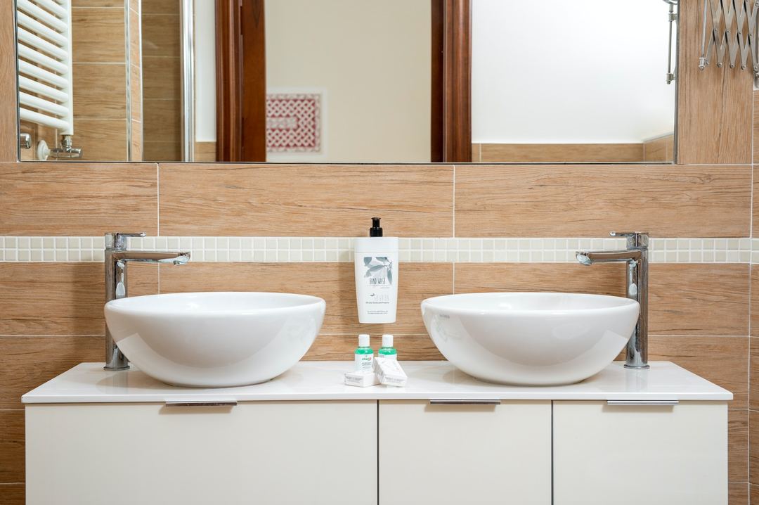 A modern bathroom vanity with dual white vessel sinks, wood-grain tile accents, and chrome fixtures in a contemporary hotel suite.