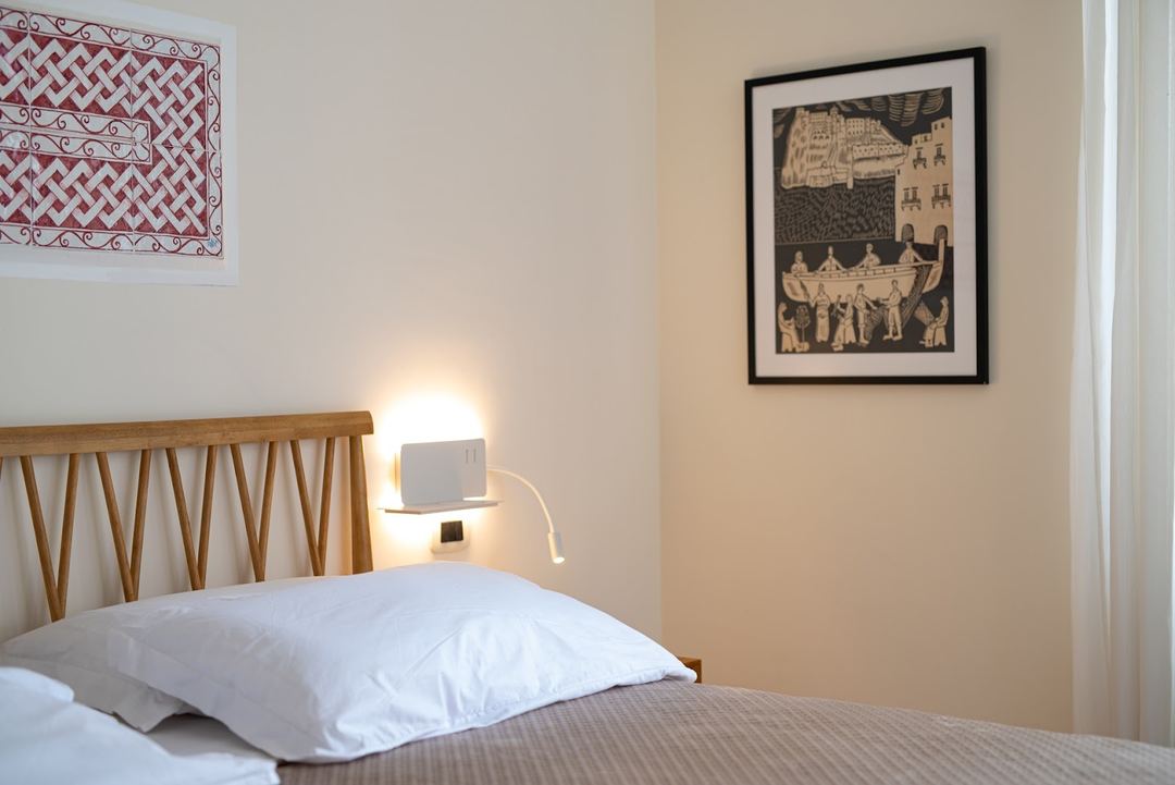 A neatly made bedroom with a wooden headboard, white pillows, bedside lamp, and framed artwork on the walls.